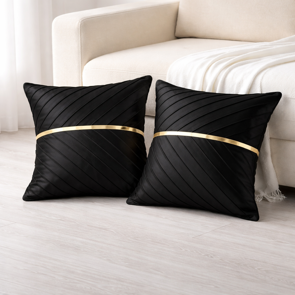 Two black pillows with gold bands on a white couch.