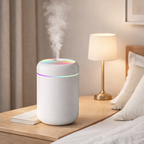 White humidifier with colorful lights on a nightstand next to a lamp and pillows.